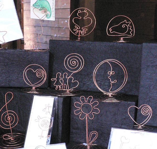 L'immagine contiene diverse figure in filo di rame che rappresentano portafoto a forma di cuore, fiore, rana, cavallo e coppietta di innamorati